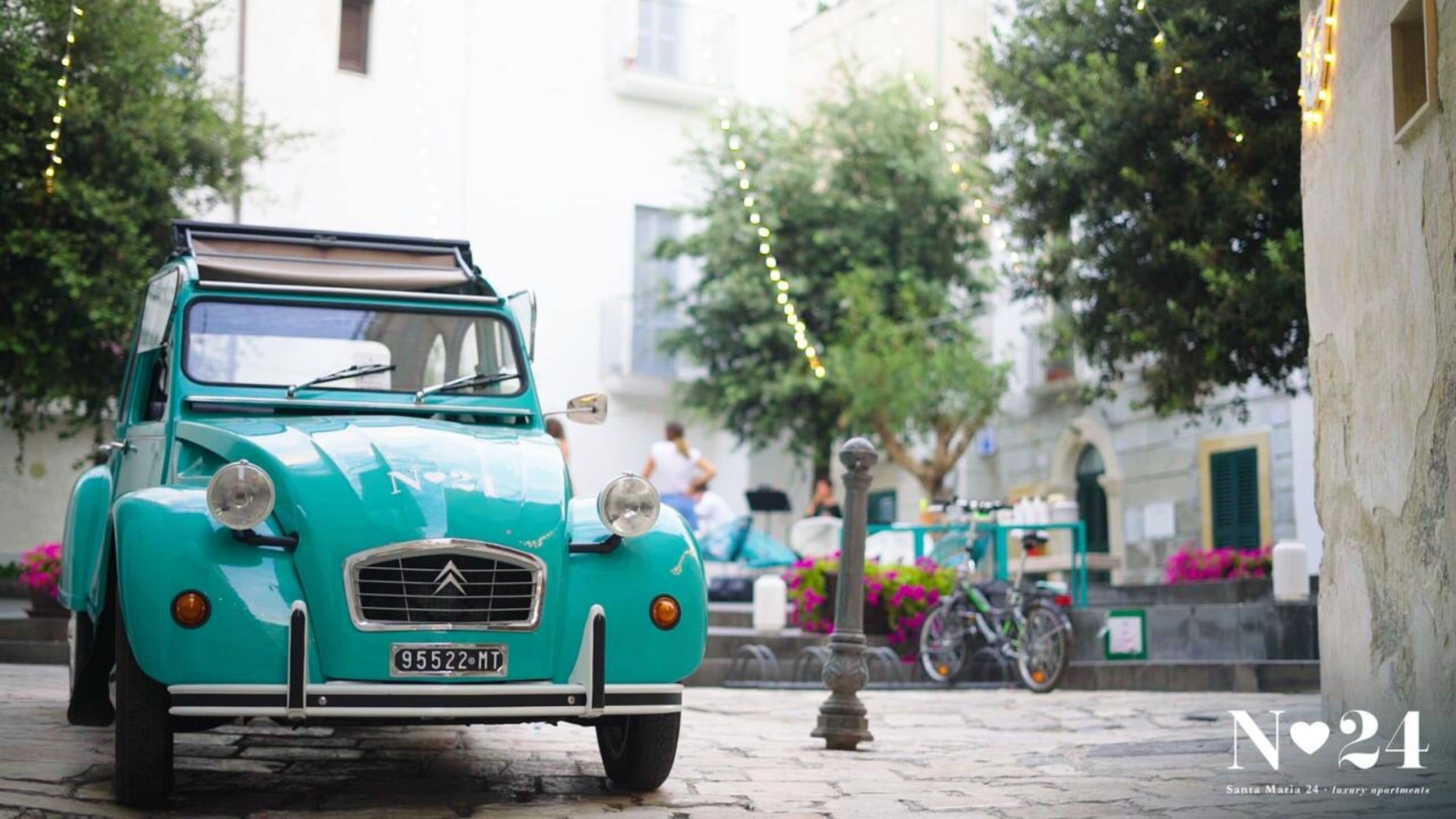 Ein türkisfarbenes Oldtimer-Auto auf einer Kopfsteinpflasterstraße mit Lichterketten.
