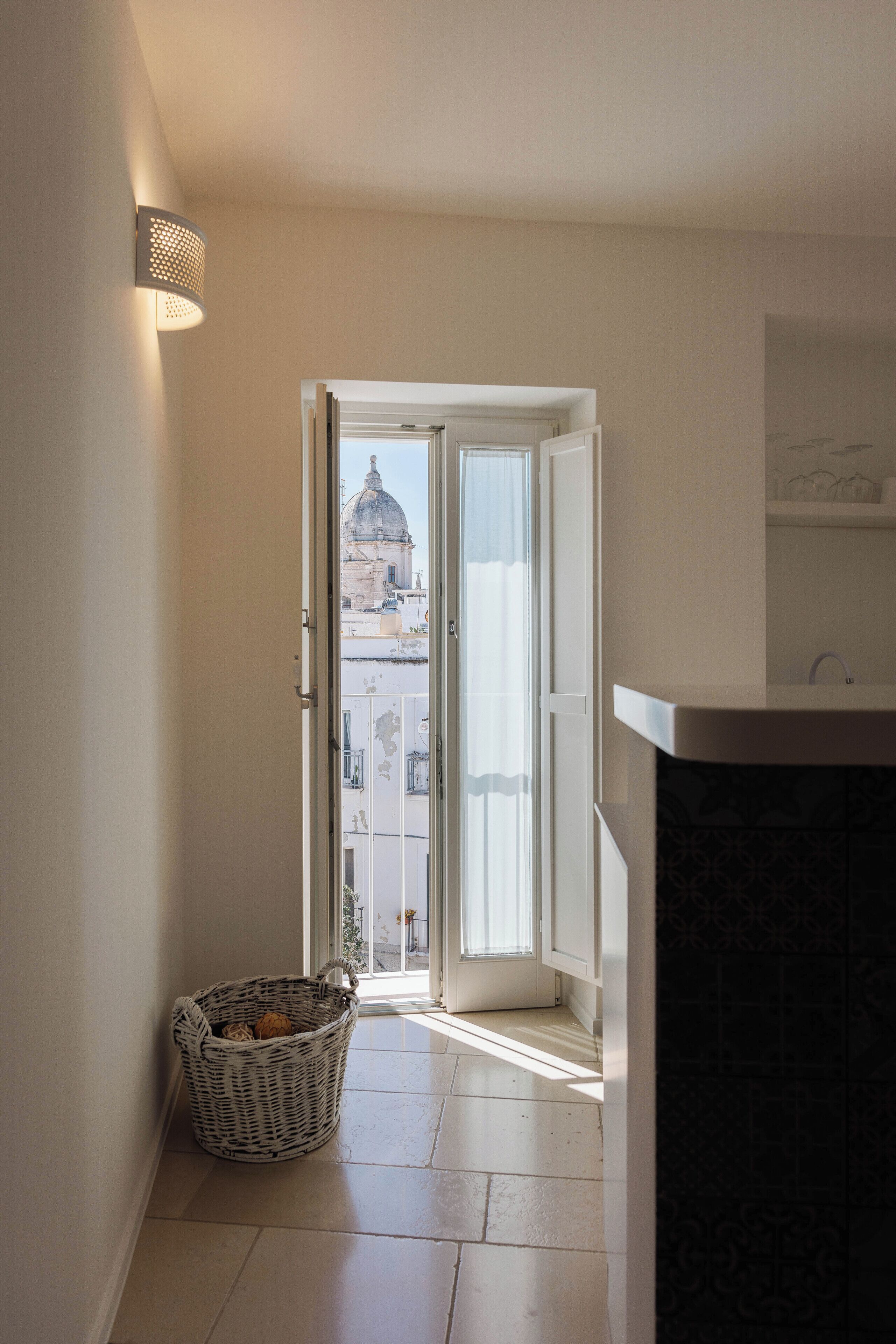 A narrow hallway with a basket, a door leading to a balcony, and a bathroom with a sink.
