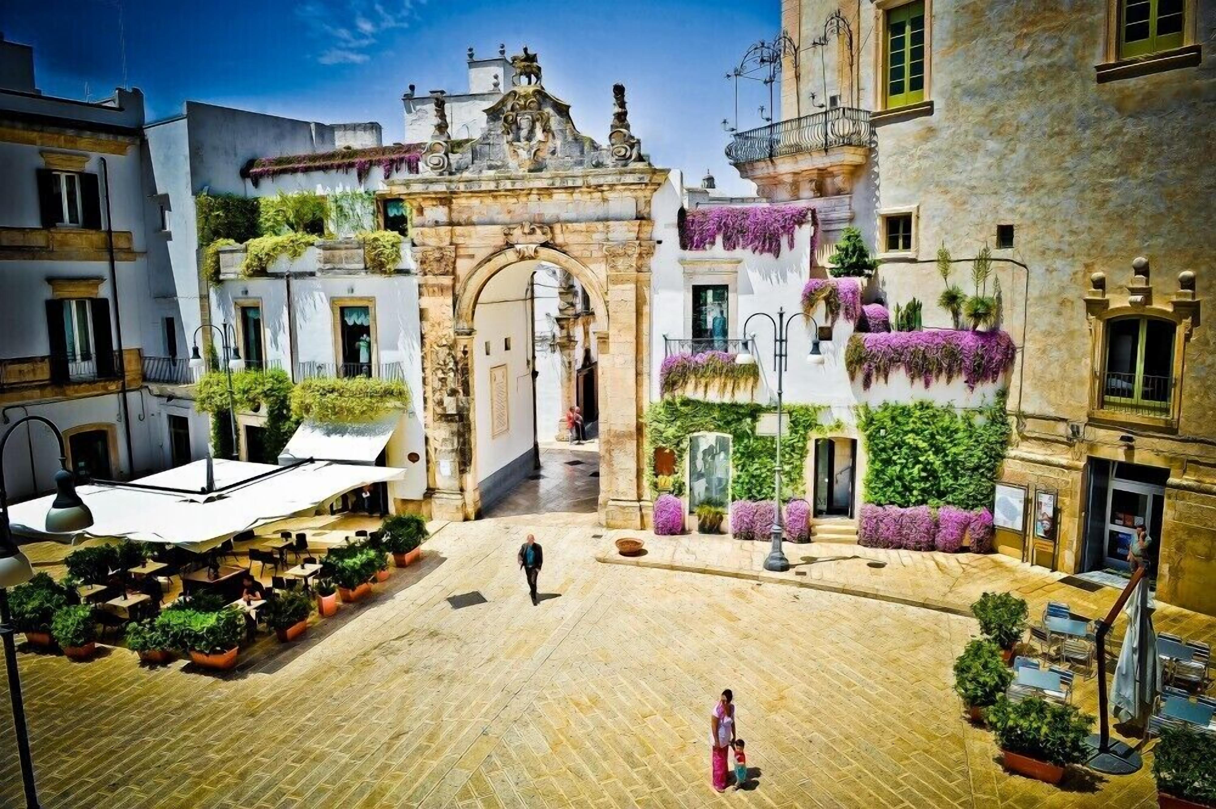 A courtyard with a central archway, potted plants, outdoor seating, and a person walking.