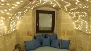 A cozy attic room with a stone wall, a wooden bench, and a cushioned bench with blue cushions. - Santa Maria 24 - Luxury Apartments (Monopoli)