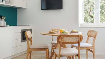 Une cuisine moderne avec des meubles blancs, un mur d’accent de couleur turquoise, un téléviseur à écran plat et un coin repas avec des chaises et une table en bois.