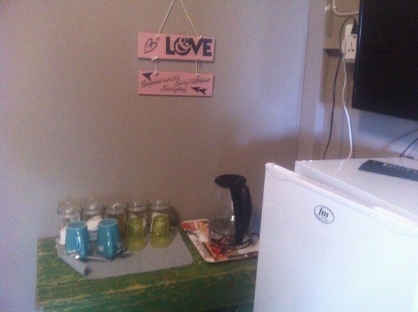 A room with a white refrigerator, a wall-mounted sign with the word "LOVE" and a heart symbol, and a table with several glasses and a black object.