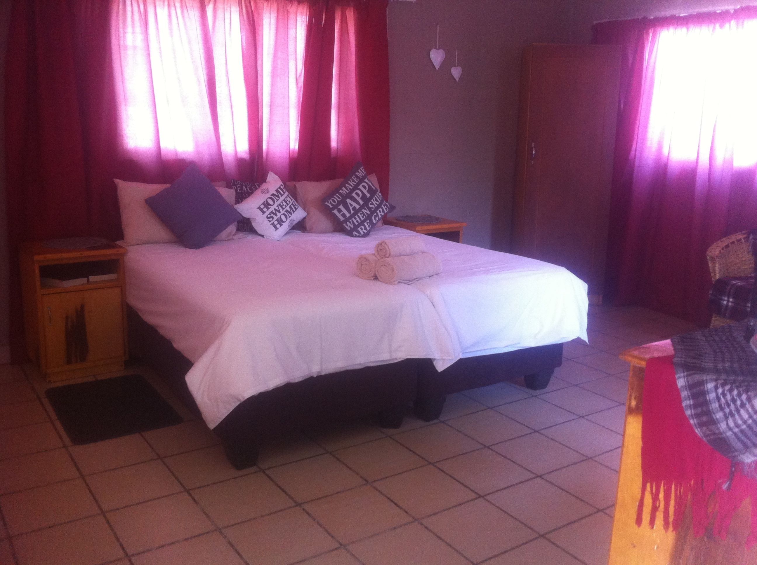 A bed with white bedding, two pillows, and a rolled towel. There are two nightstands with a small table and a chair.