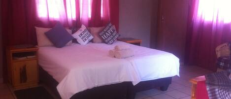 A bed with white bedding, two pillows, and a rolled towel. There are two nightstands with a small table and a chair.