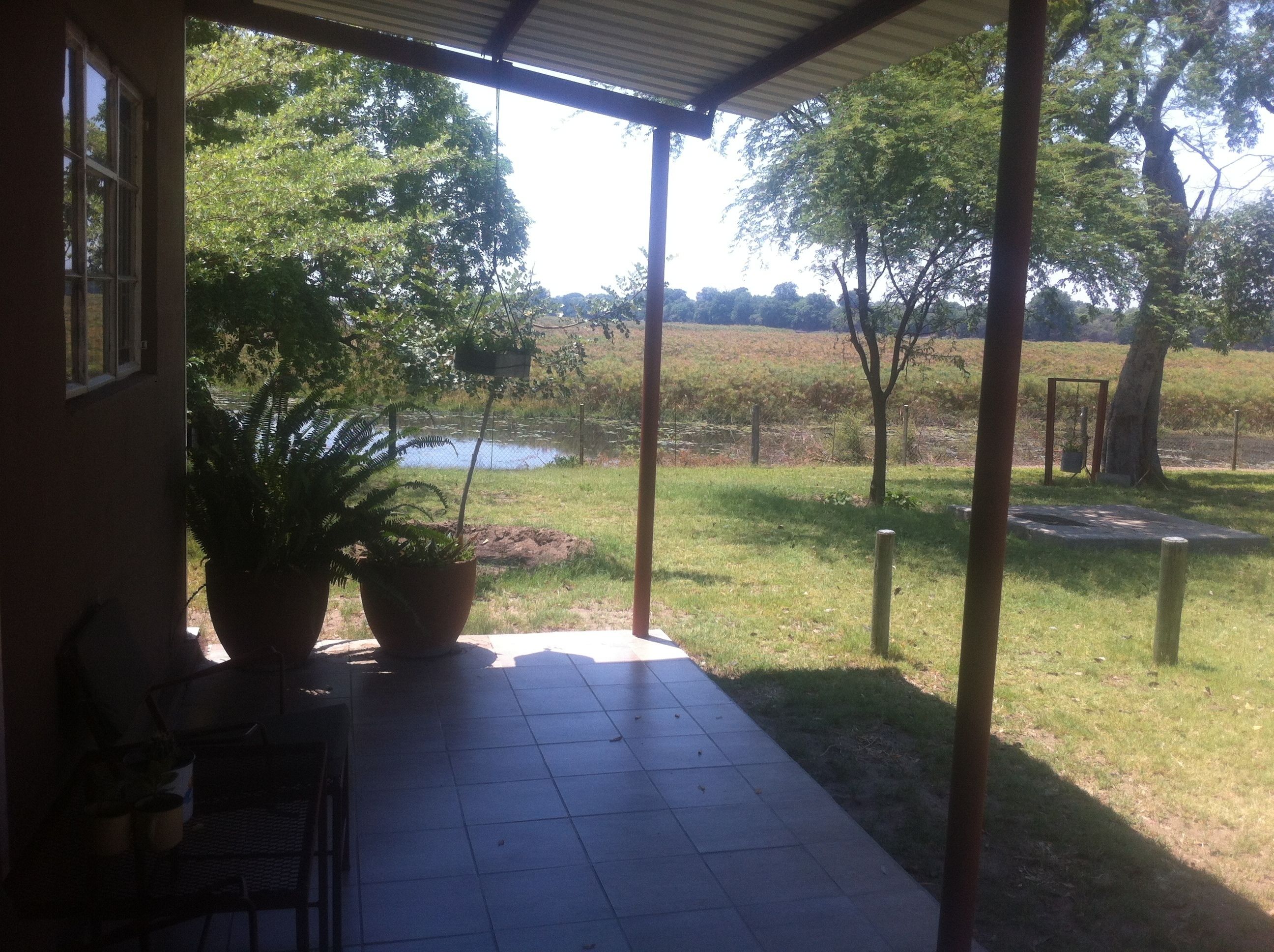 A covered patio with potted plants, a view of a grassy area, and a body of water in the distance.