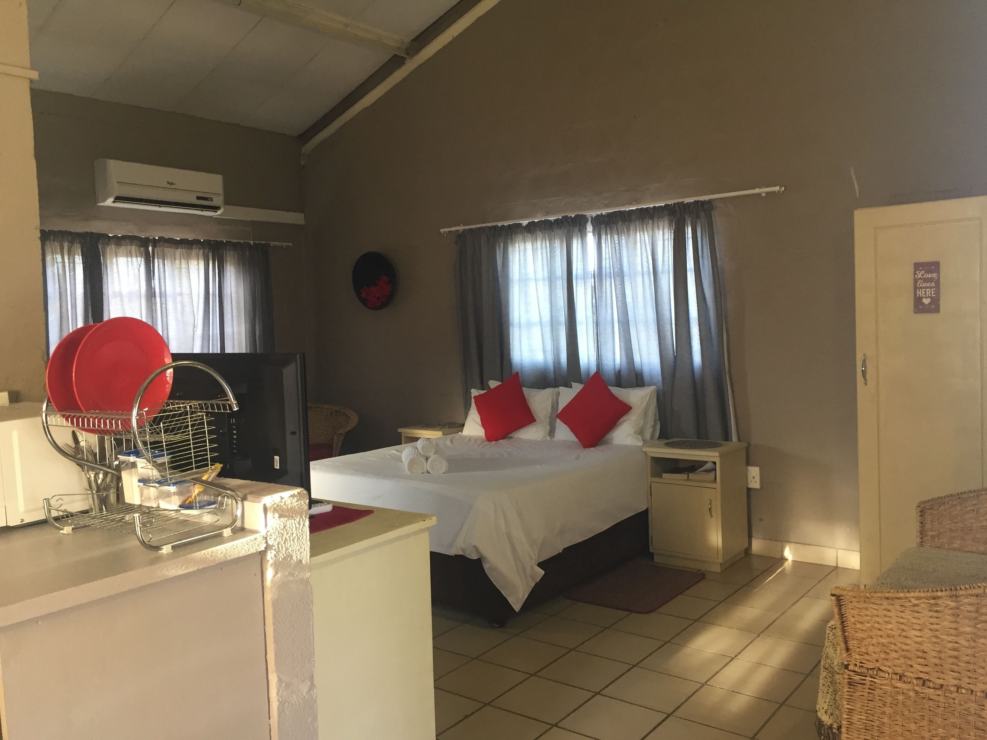 A hotel room with a bed, a TV, a desk with a dish rack, and a window with curtains.