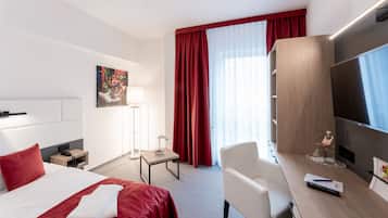 Une chambre d’hôtel comprenant un lit, un bureau avec une télévision, une chaise, une table de chevet et une fenêtre avec des rideaux.