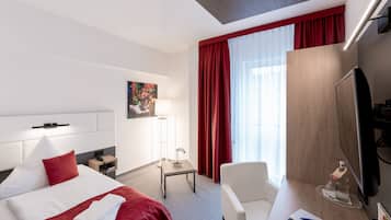 A hotel room with a bed, a desk, a chair, a TV, and a window with curtains.