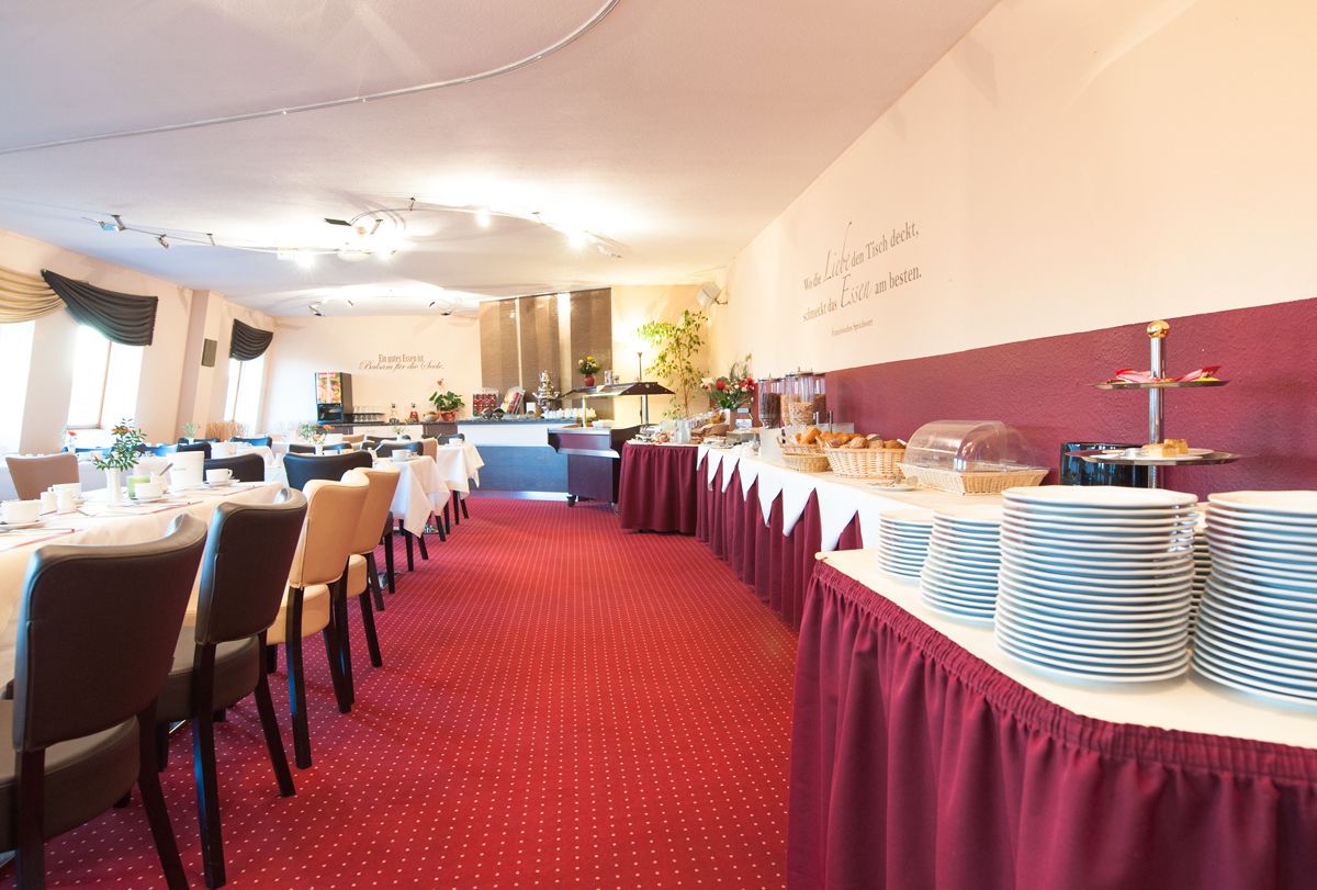 Une salle de banquet avec des tables rondes, un espace buffet et un sol recouvert d’un tapis rouge.