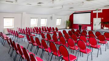 Ein Konferenzraum mit Reihen roter Stühle, einer Whiteboard-Tafel und einer Projektionsleinwand.