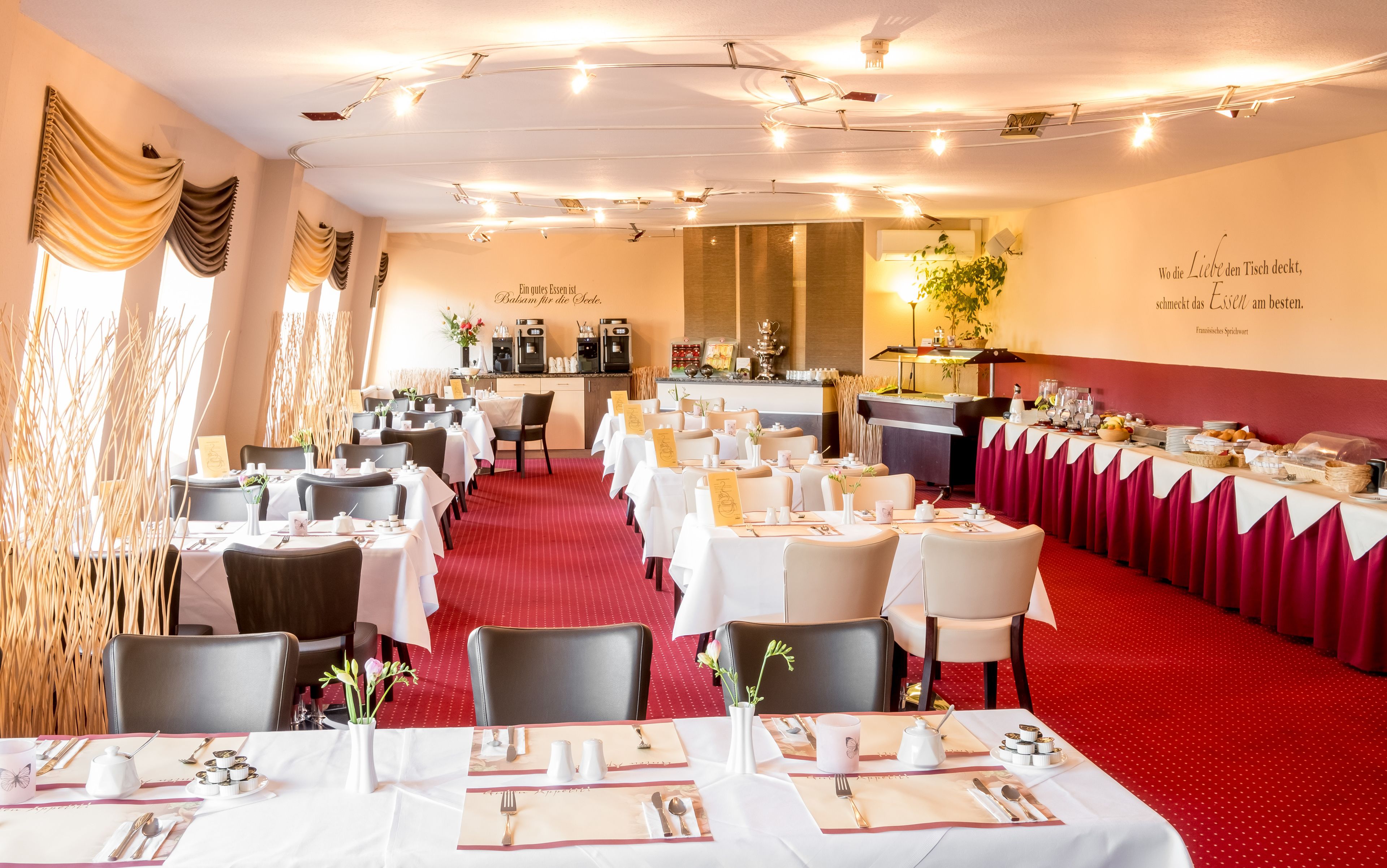 Un comedor formal con mesas dispuestas para el servicio, una zona de bar y una pared decorativa con una cita.