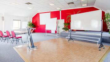 A spacious room with a red accent wall, a whiteboard, a podium, and a seating area with chairs.