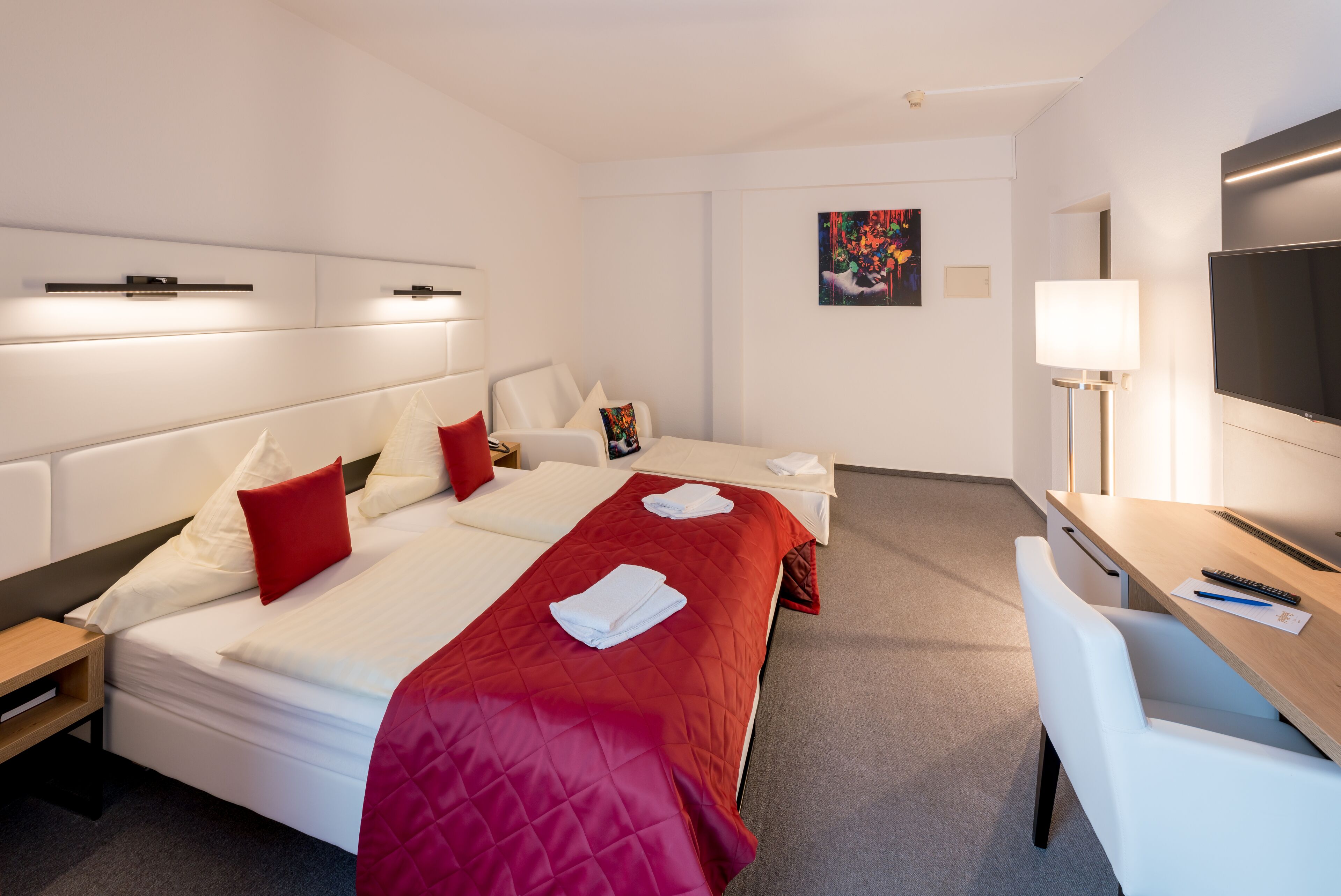 A hotel room with two beds, a desk, a TV, and a painting on the wall.