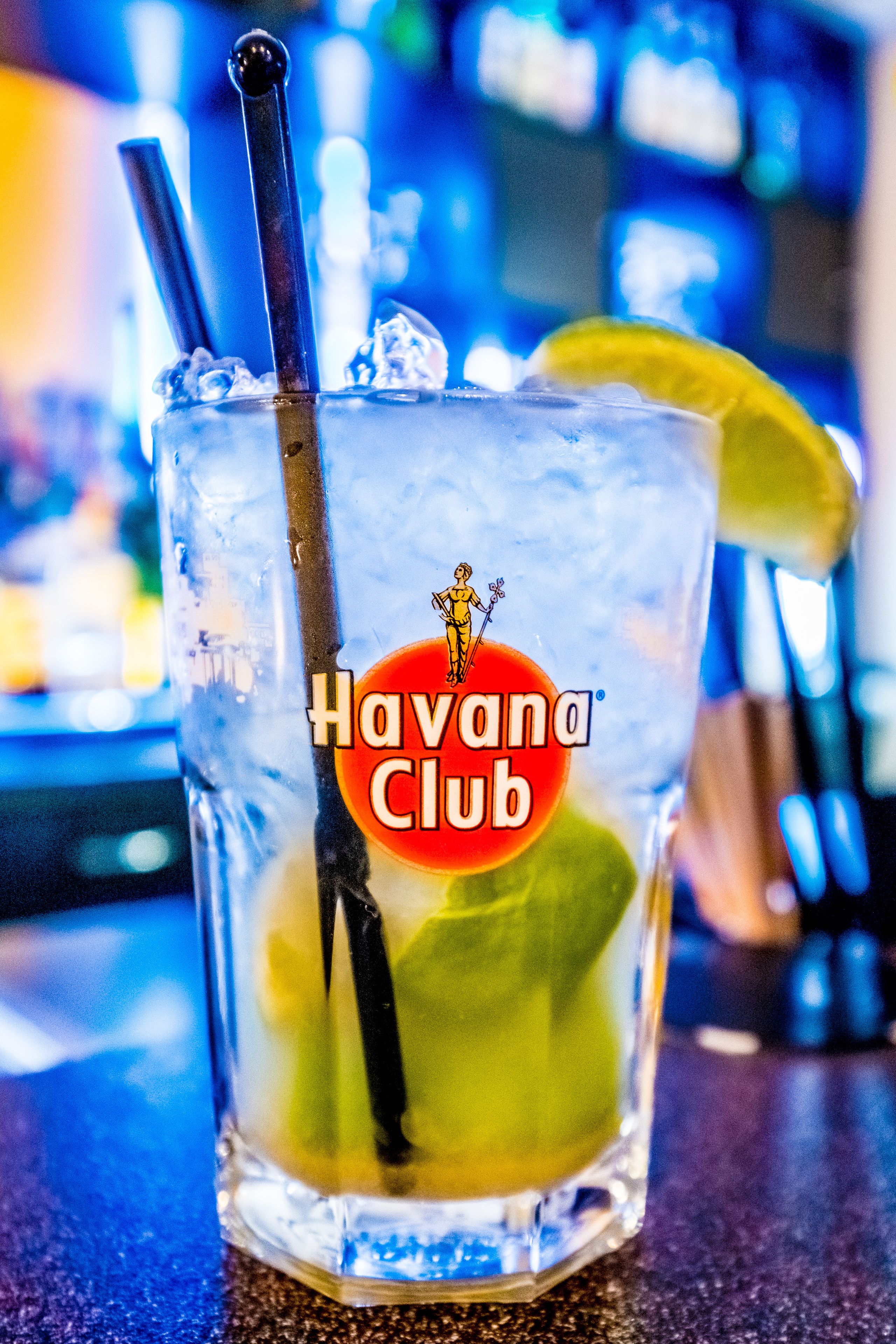 Ein Glas mit Trinkhalm und Limettenspalte, beschriftet mit "Havana Club", auf einer Bar.