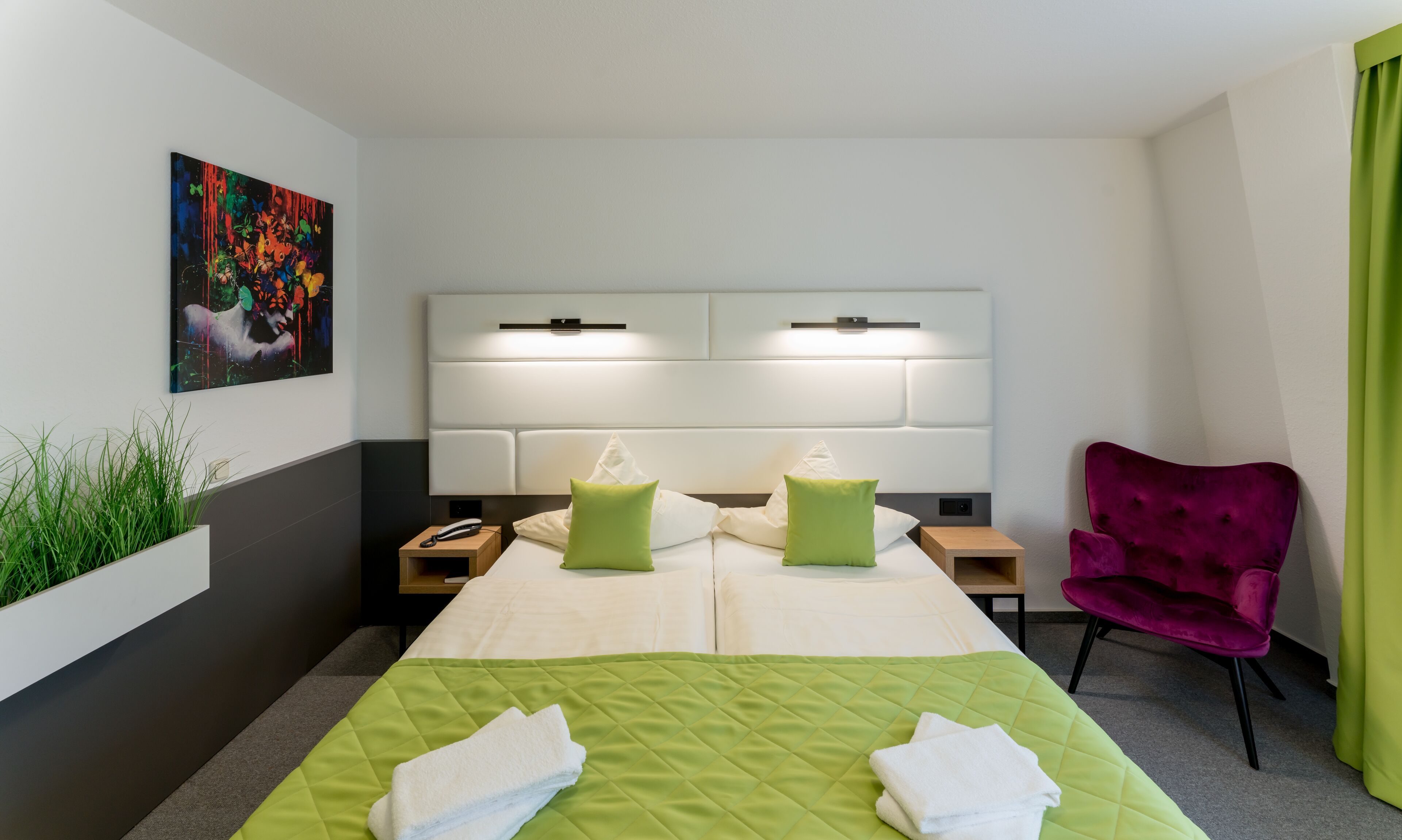 Una habitación de hotel con una cama grande, dos mesitas de noche, una lámpara de noche, una silla, un cuadro en la pared y una cortina verde.