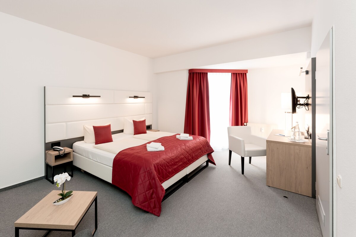 Una habitación de hotel moderna con una cama grande, un escritorio, una silla y una pequeña mesa con una flor.