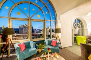A room with a large arched window featuring star decorations, two teal armchairs with red cushions, a small table with a vase and candle, and a bright green chair. - Hotel Stadtfeld (Magdeburg)