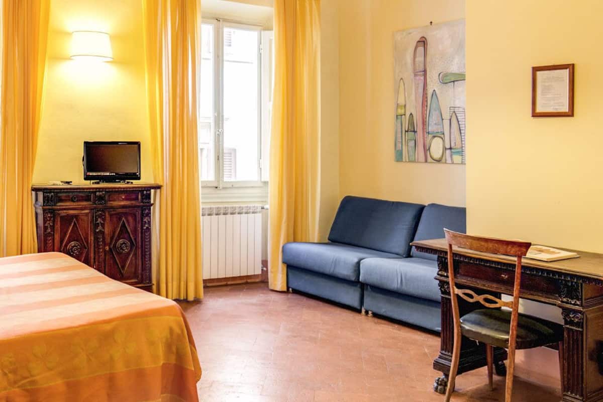 Et hotelværelse med seng, sofa, skrivebord med stol, fjernsyn og et billede på væggen.