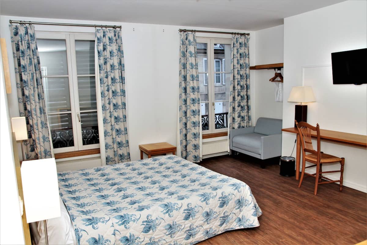 Ein Hotelzimmer mit einem Bett, einem Schreibtisch, einem Sessel, einem Fernseher und einem Fenster mit Vorhängen.