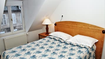 A bedroom with a sloped ceiling, a bed with a floral bedspread, a bedside lamp, and a window with shutters.