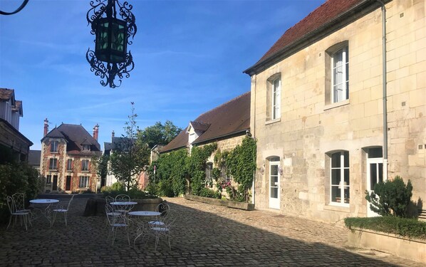 A cobblestone courtyard with outdoor seating and a historic building with stone walls and windows. - Hotel Le Regent (Villers-Cotterets)