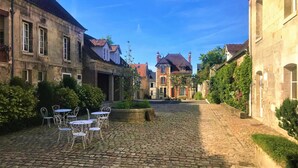 A cobblestone street with historic buildings, outdoor seating, and a clear sky. - Hotel Le Regent (Villers-Cotterets)
