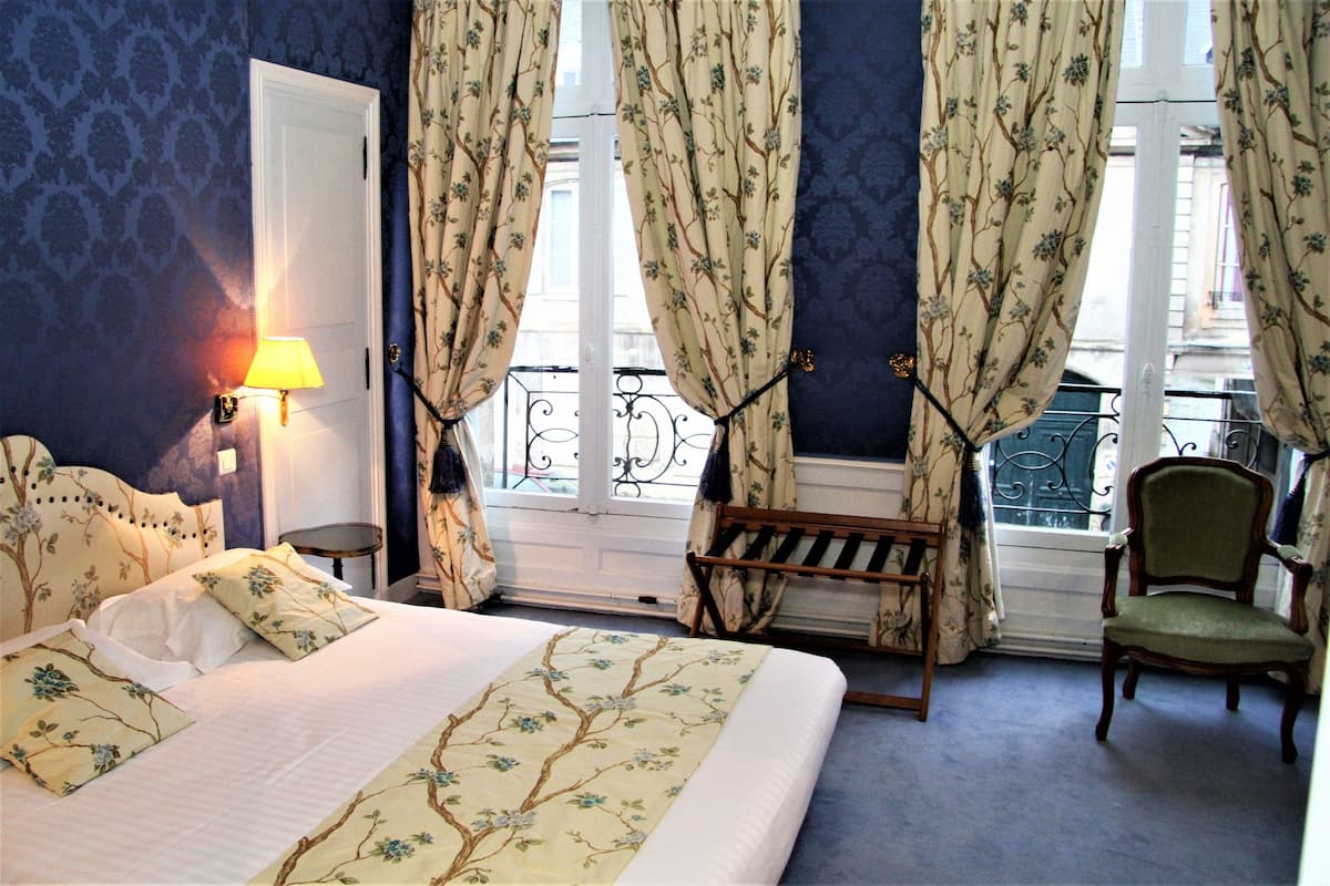 Ein Schlafzimmer mit einem Bett, einem Sessel, einer Bank und Vorhängen.