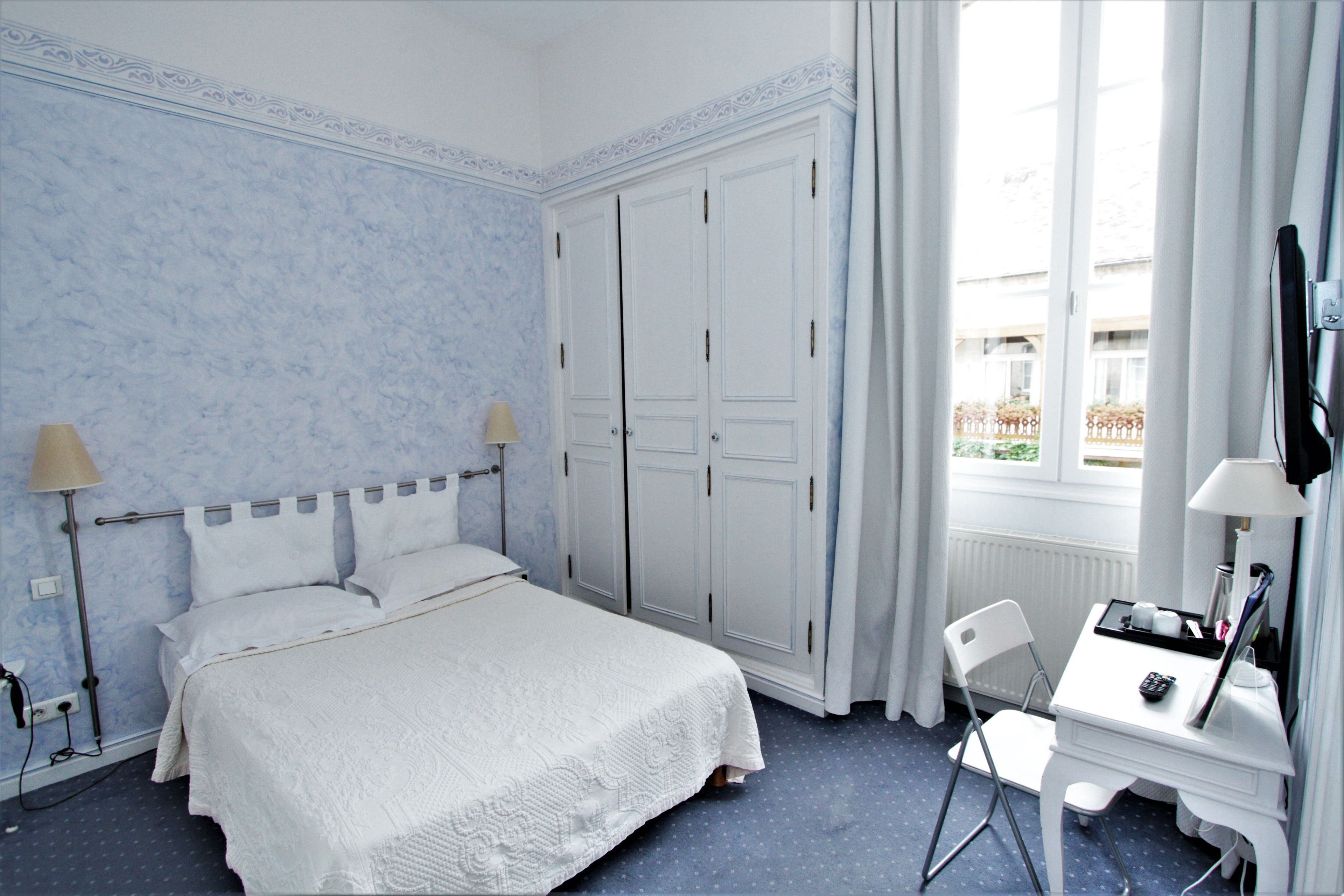 A hotel room with a bed, a desk, a chair, a TV, and a window with curtains.