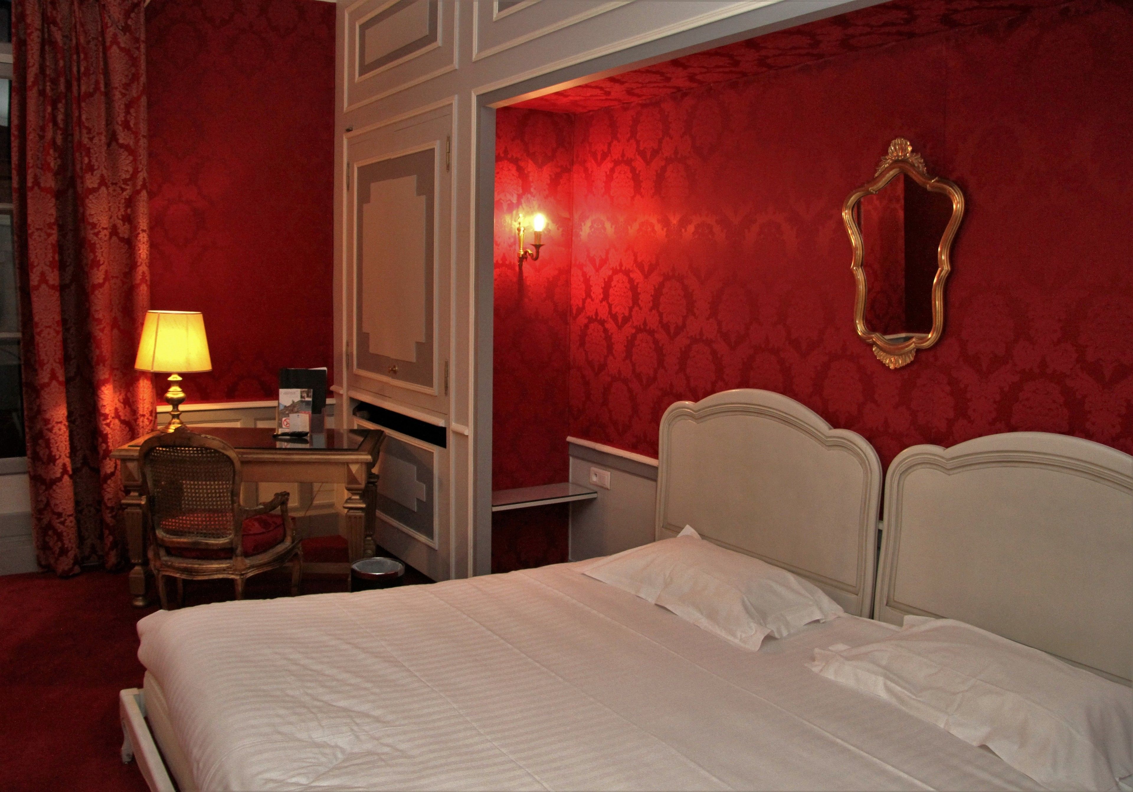 Ein Hotelzimmer mit einem Bett, einem Schreibtisch mit Lampe, einem Sessel und einem Spiegel an der Wand.