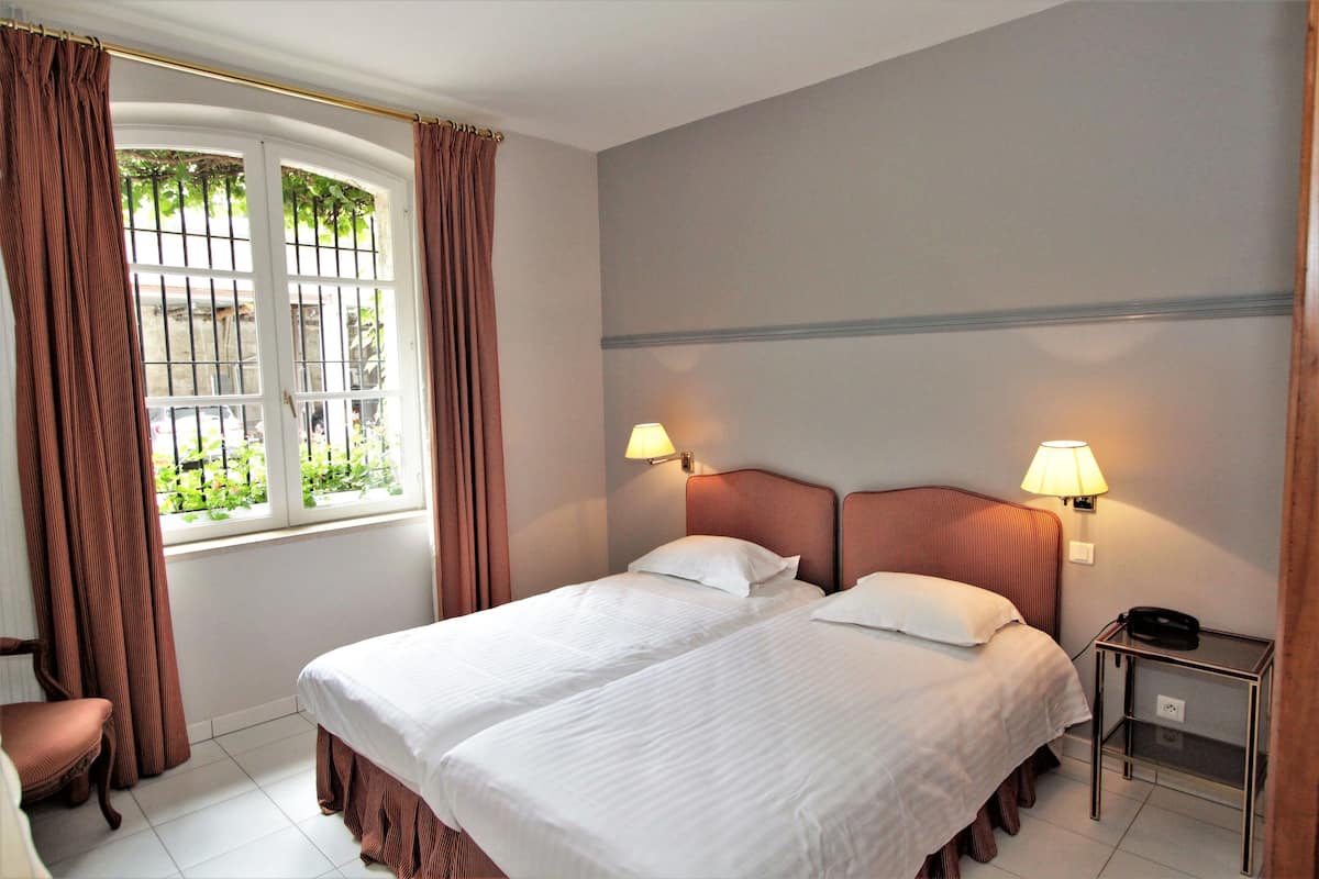 Ein Hotelzimmer mit zwei Betten, einem Fenster mit Vorhängen, einem Nachttisch mit Lampe und einem Sessel.