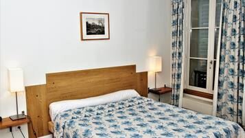 Una cama bien hecha con cubrecama floral, cabecera de madera, lámparas de noche y un cuadro en la pared.