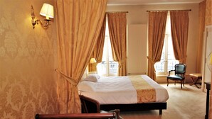 A hotel room with a bed, a chair, a lamp, and curtains. - Hotel Le Regent (Villers-Cotterets)