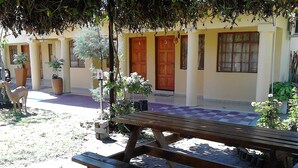 A wooden bench in a shaded outdoor area with a building in the background.