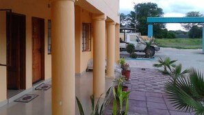 A building with a covered entrance, columns, and a paved area with potted plants.