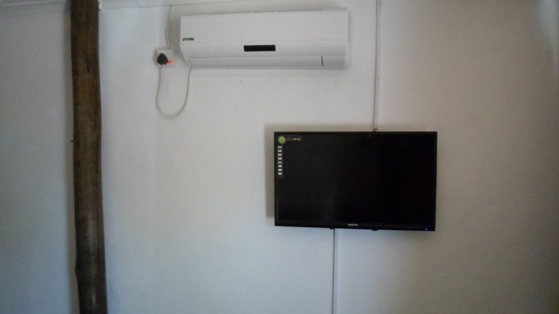 A white wall with a black electronic device and a white air conditioning unit mounted on it.