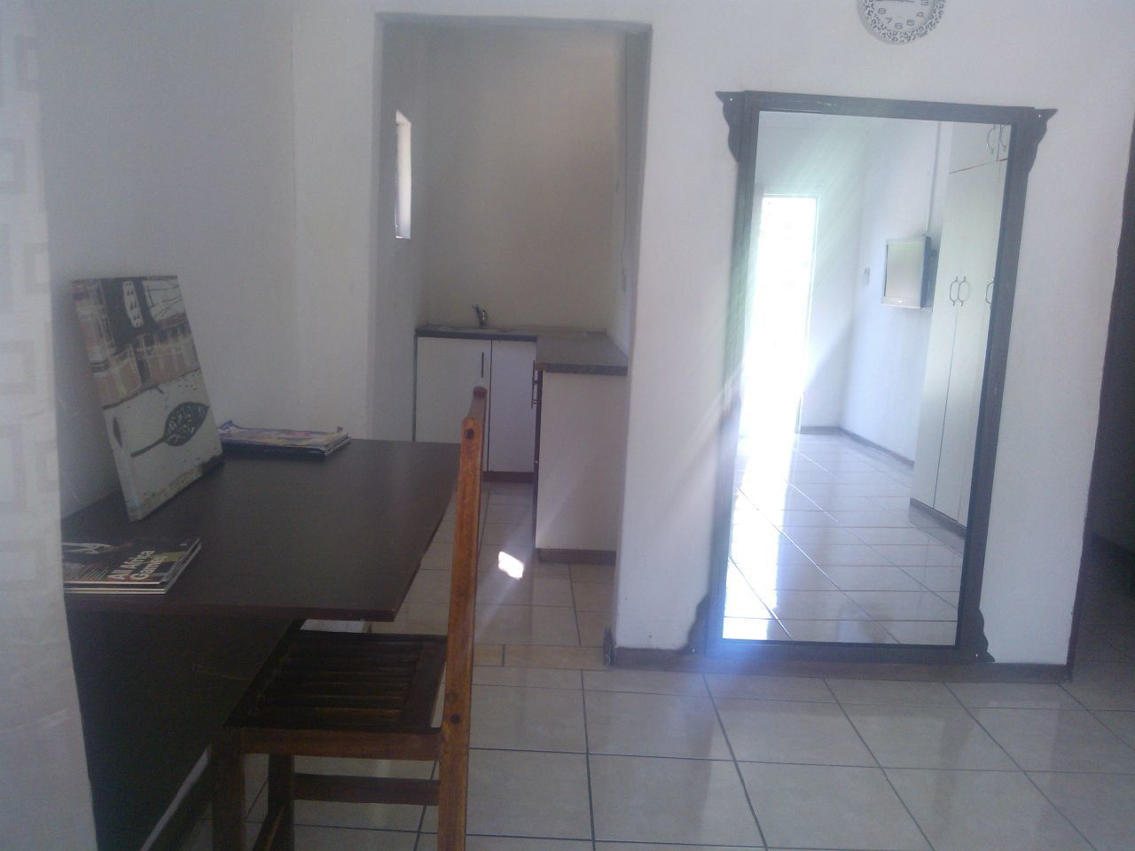 Comedor con mesa y sillas de madera, kitchenette pequeña y vista a un pasillo que lleva a un baño.