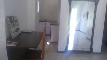 Comedor con mesa y sillas de madera, kitchenette pequeña y vista a un pasillo que lleva a un baño.