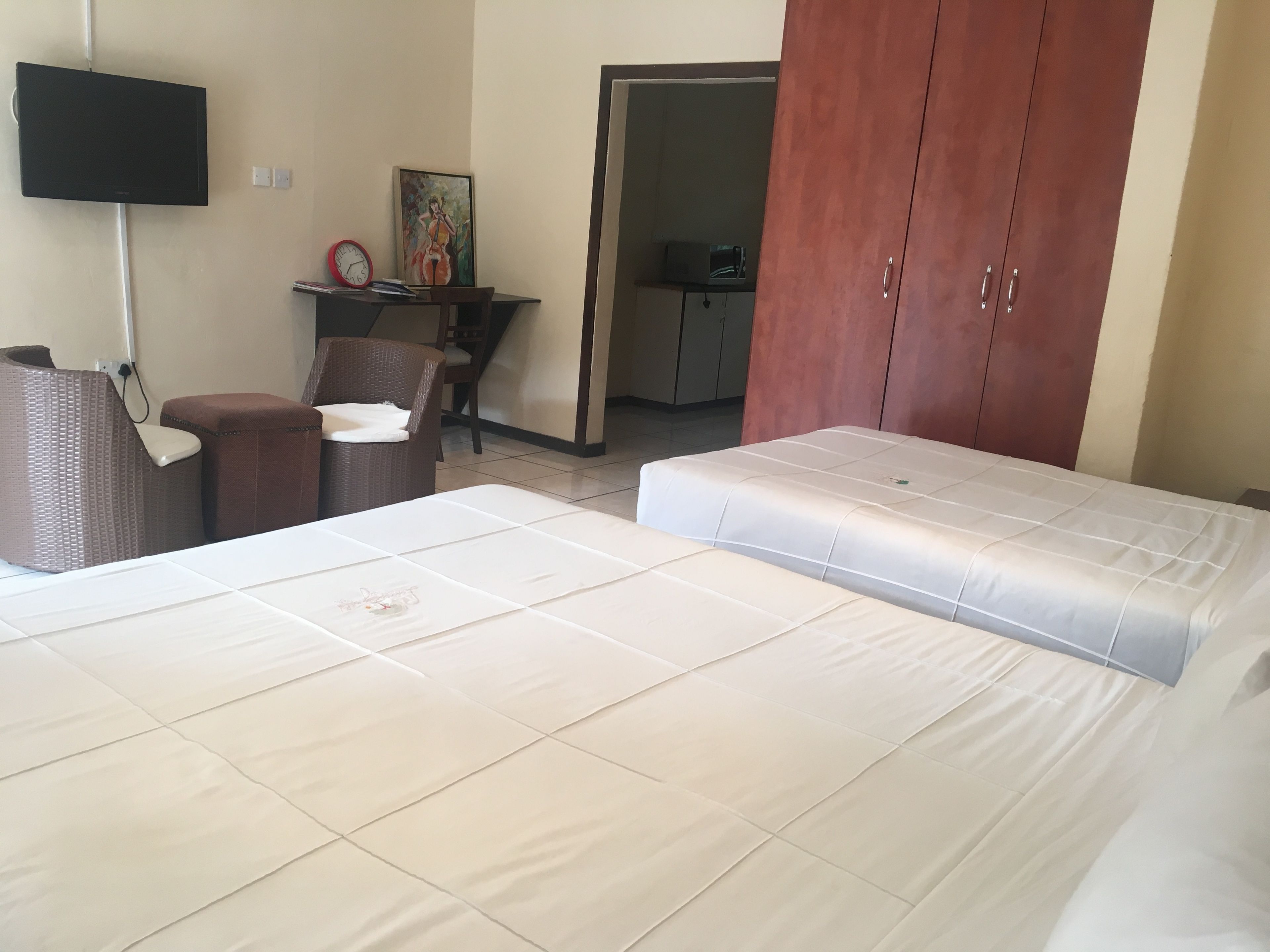 Habitación de hotel con una cama, una silla, una mesita, un televisor montado en la pared y un armario.