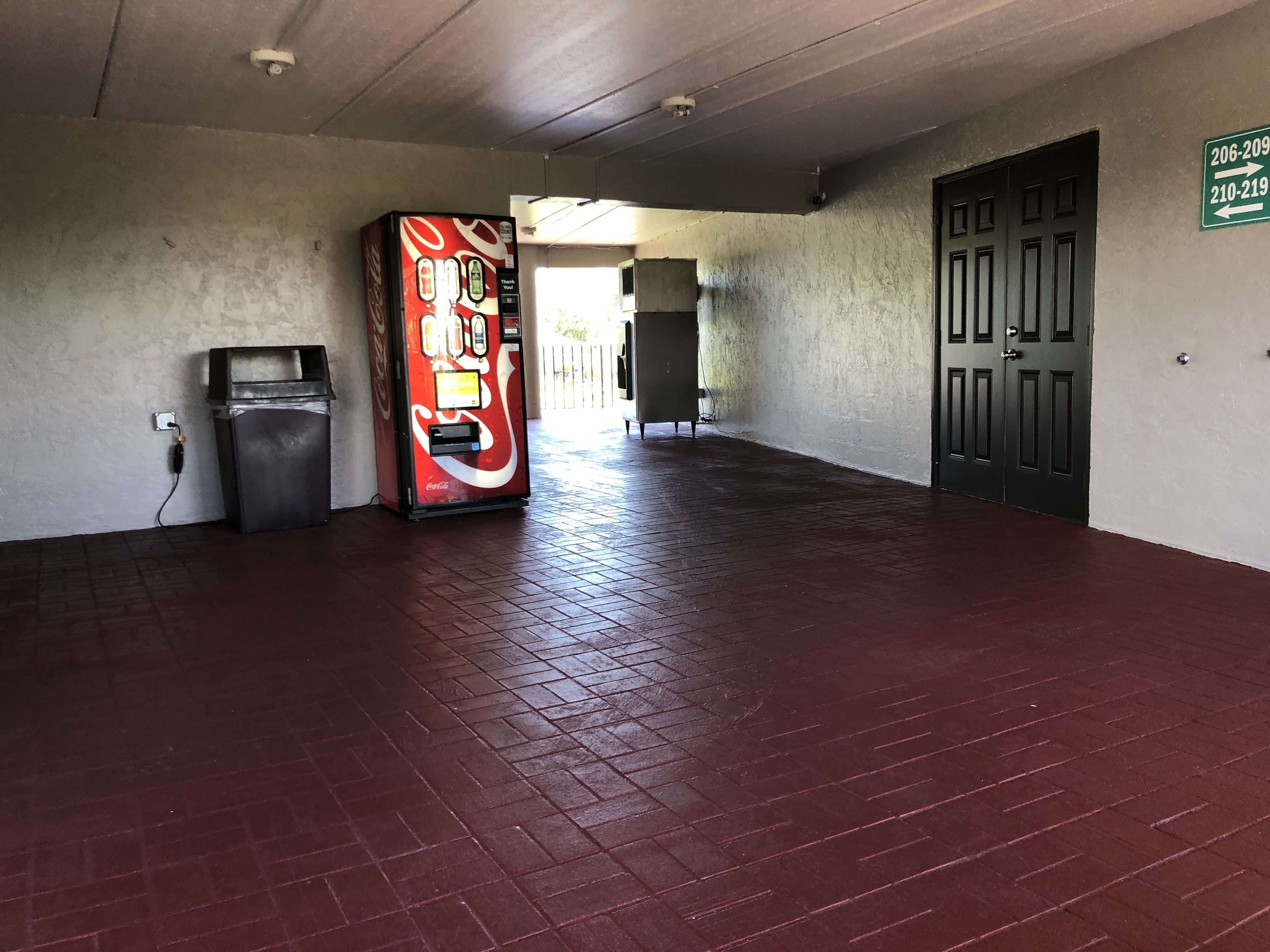 A hallway with a vending machine, a trash bin, and a door with directional signs.