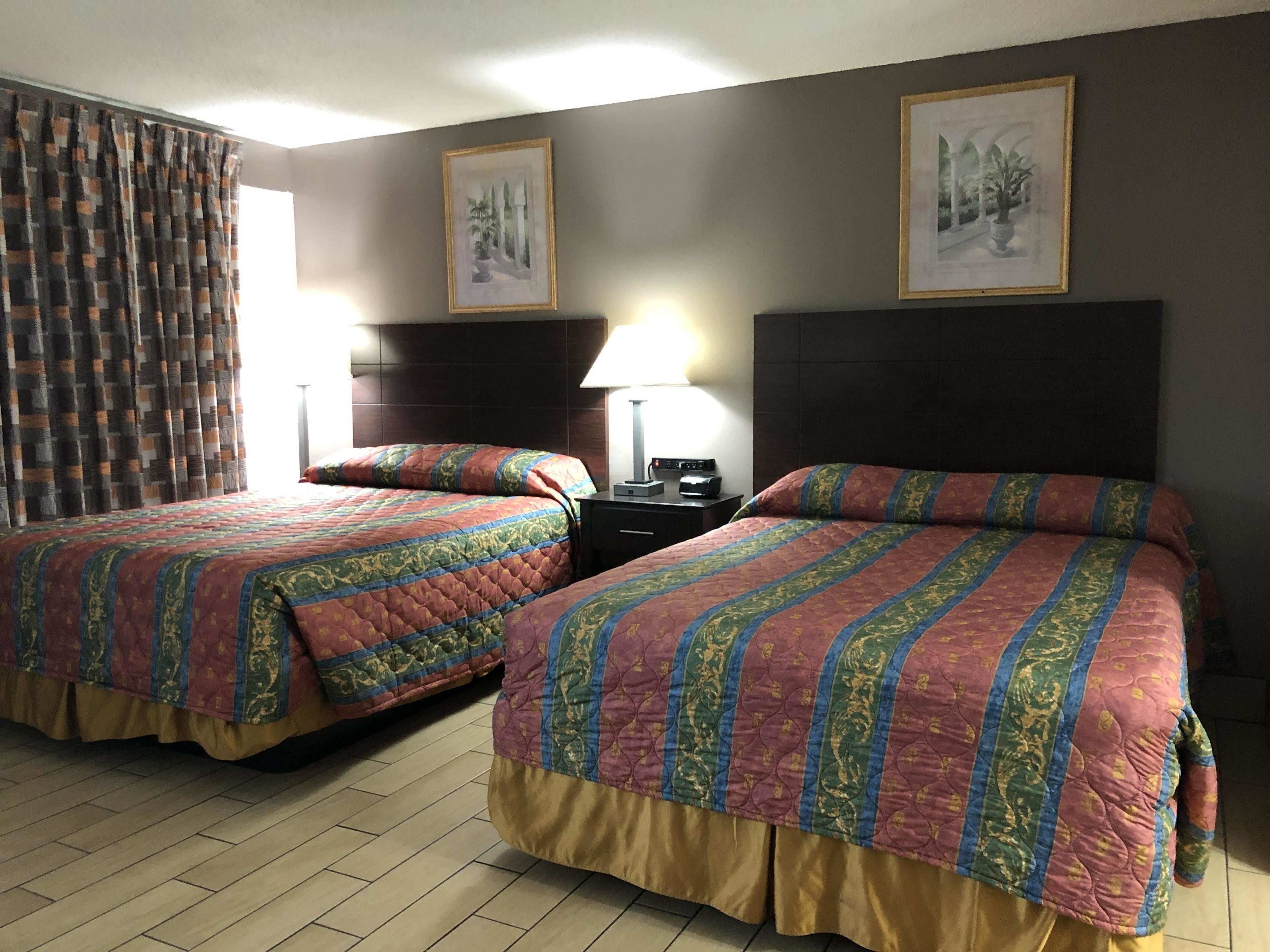 Ein Hotelzimmer mit zwei Betten, einem Nachttisch, einer Lampe und zwei gerahmten Bildern an der Wand.