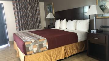 A hotel room with a large bed, two bedside lamps, a nightstand, a desk with a lamp, a painting on the wall, and a window with curtains.