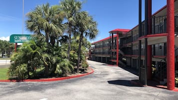 Un motel de varios pisos con fachada roja y blanca, palmeras y cielo despejado.