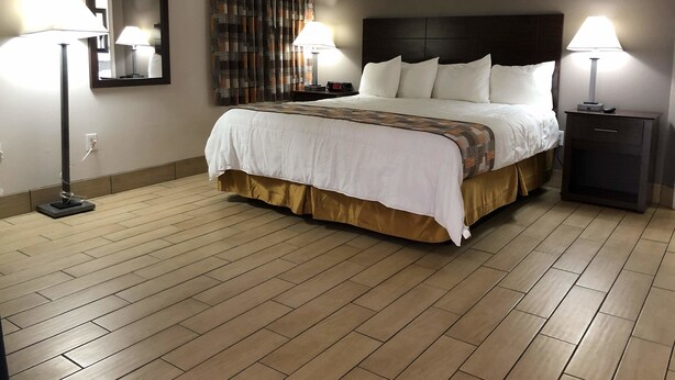 A hotel room with a large bed, two bedside lamps, a nightstand, a mirror, and a curtain. - Sun Coast Inn (Englewood)