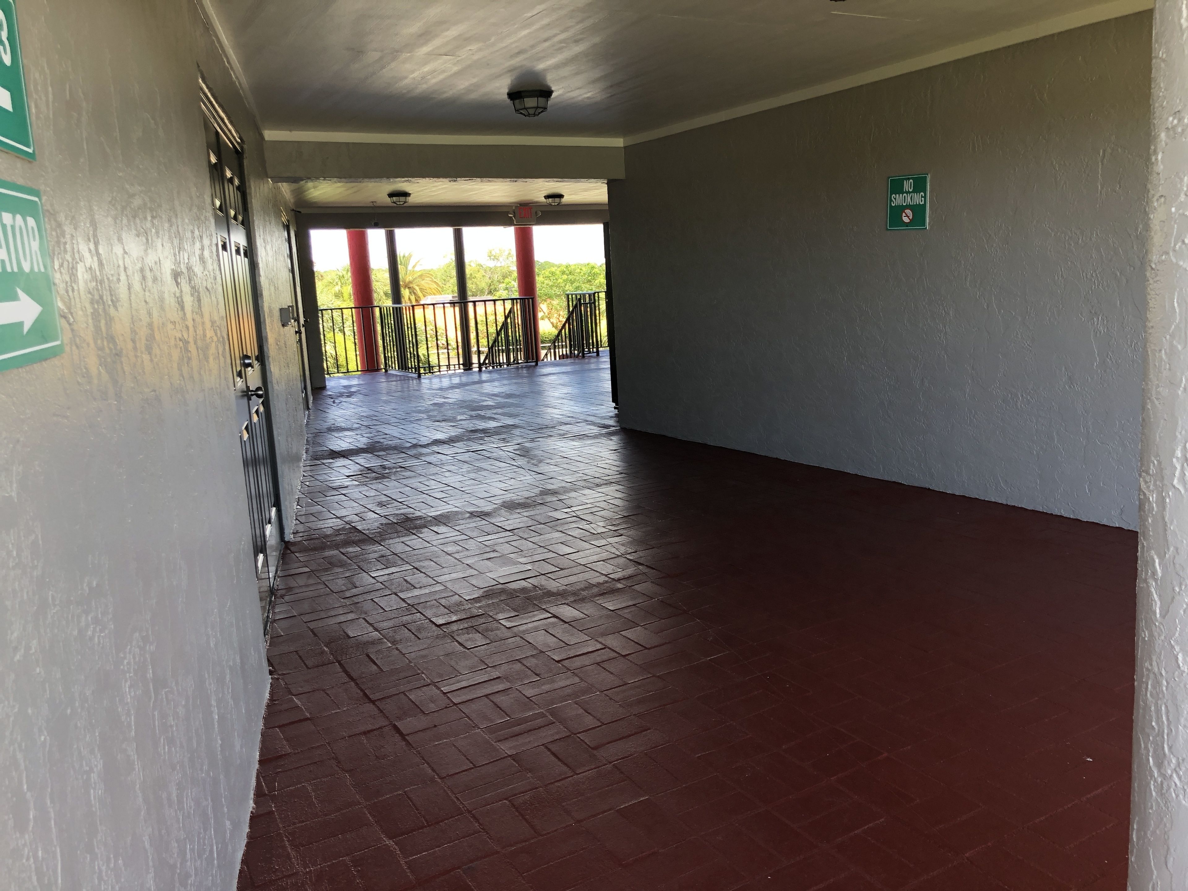 A corridor with a red brick floor, a green exit sign, and a 'No Smoking' sign.