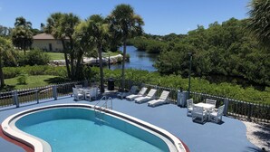 A swimming pool with a deck, lounge chairs, and a view of a river. - Sun Coast Inn (Englewood)