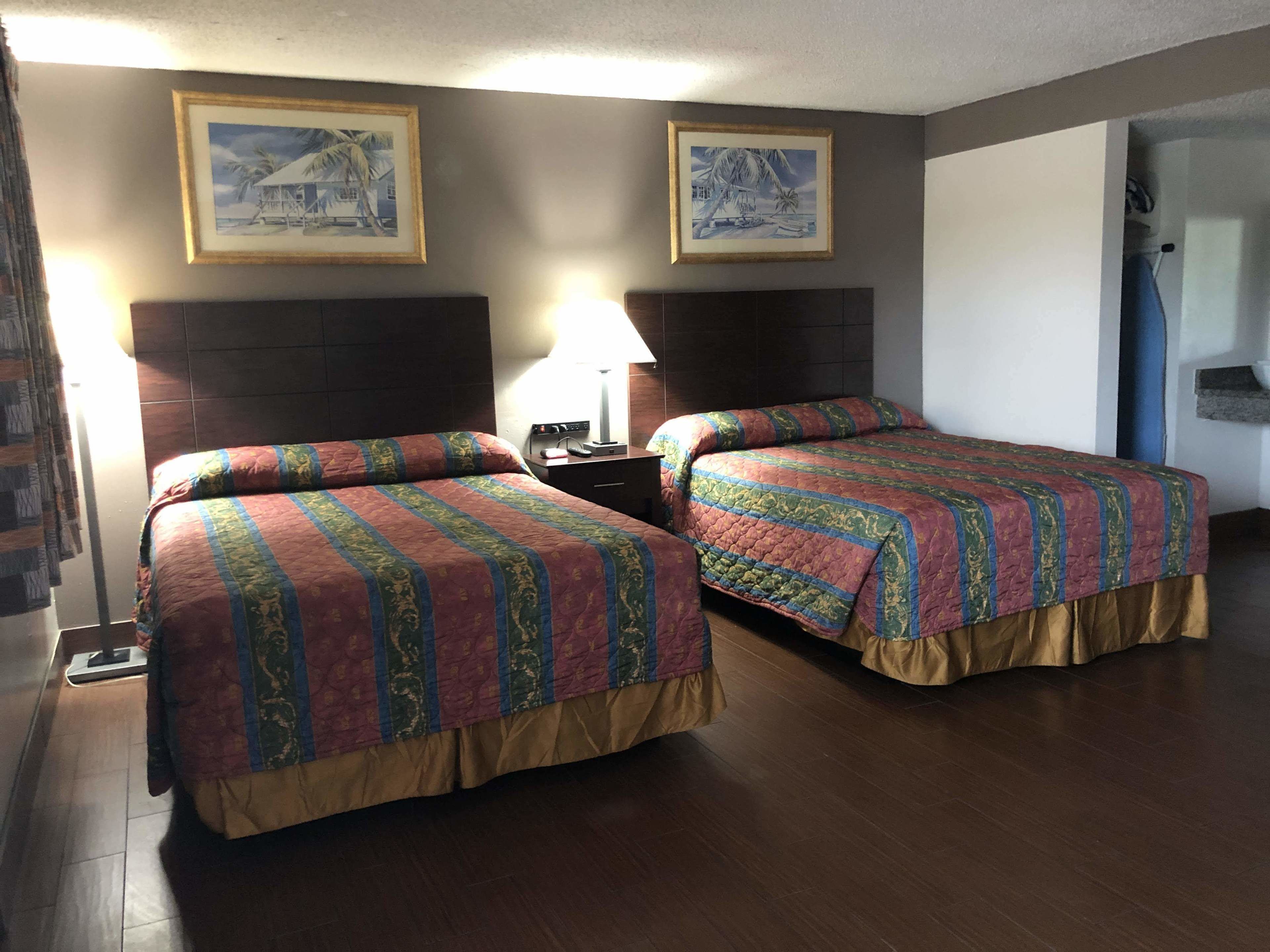A hotel room with two beds, a nightstand, a lamp, and two framed pictures on the wall.