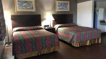 A hotel room with two beds, a nightstand, a lamp, and two framed pictures on the wall.
