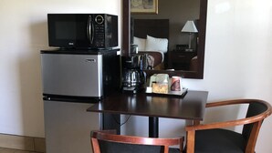 A compact kitchenette with a refrigerator, microwave, and coffee maker. There is a wooden table with two chairs and a mirror above it. - Sun Coast Inn (Englewood)