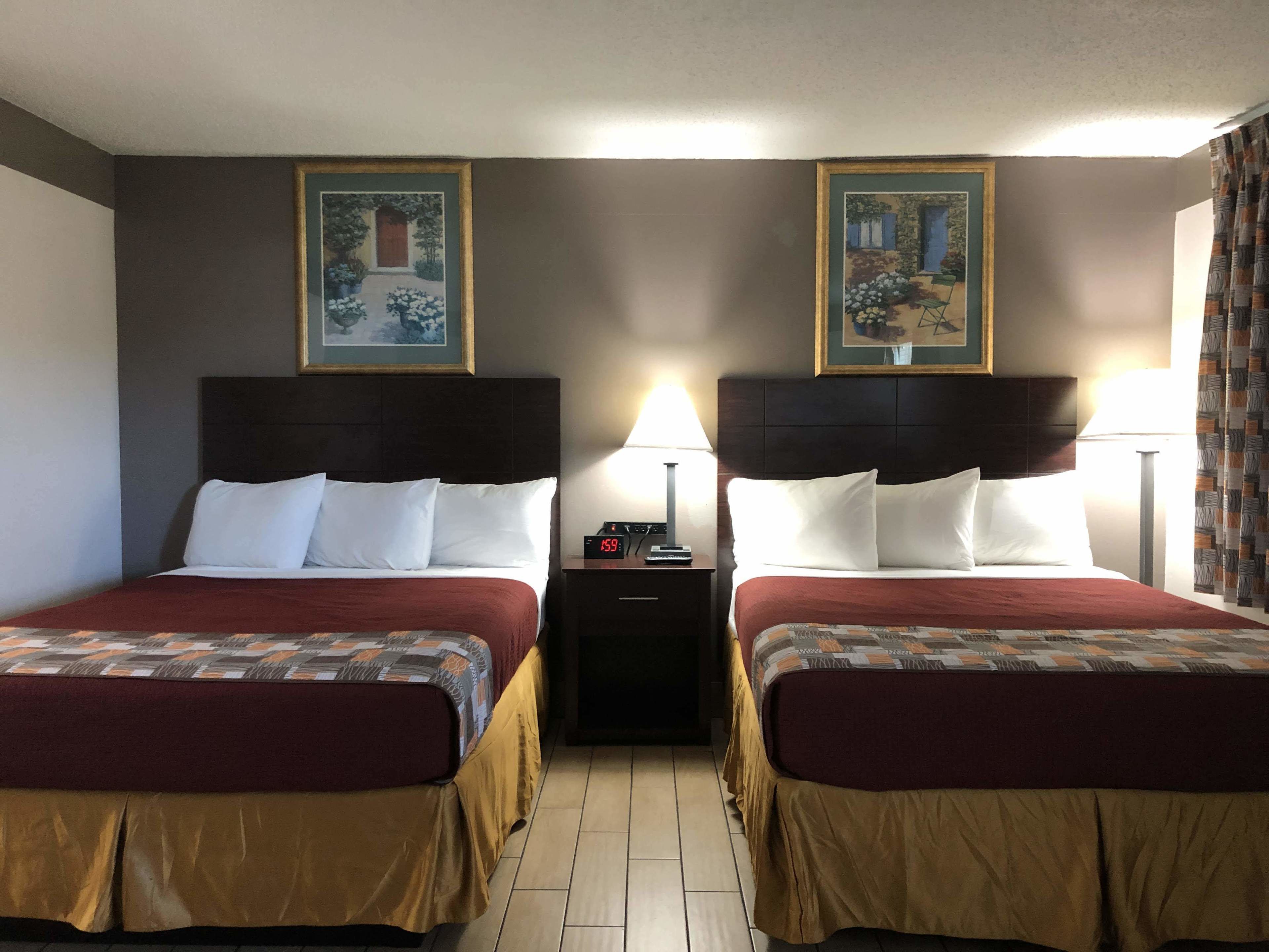 Habitación de hotel con dos camas, cada una con cabecera, mesita de noche con un reloj y cuadros en las paredes.