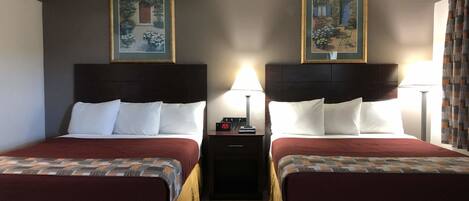 A hotel room with two beds, each with a headboard, a nightstand with a clock, and framed pictures on the walls.